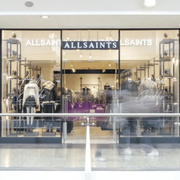 Façade d'une boutique AllSaints avec vêtements exposés derrière de grandes vitrines transparentes.