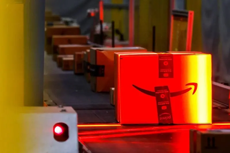 Colis Amazon sur un tapis roulant éclairé par une lumière rouge dans un centre de distribution