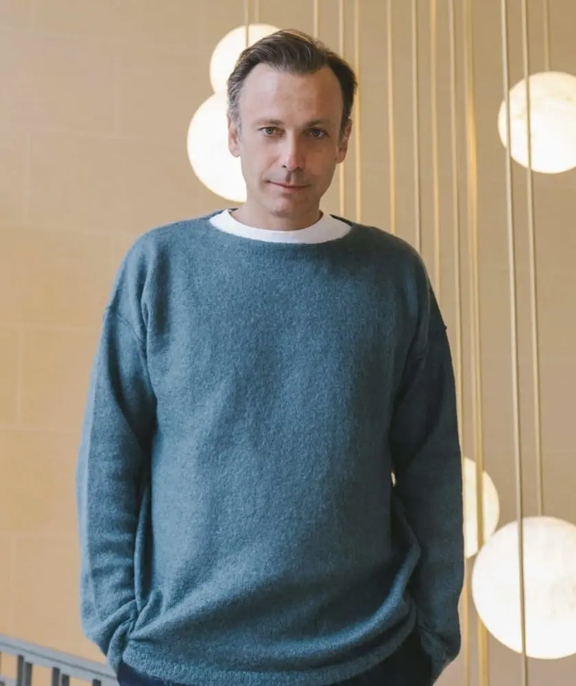 Homme en pull bleu debout devant des lampes suspendues, évoquant la stratégie de Cavalli aux USA