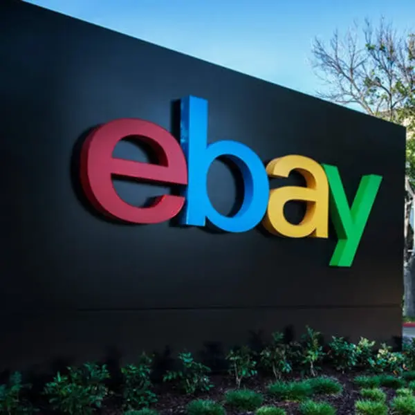 Logo coloré d'eBay sur un panneau noir entouré de verdure et d'arbres