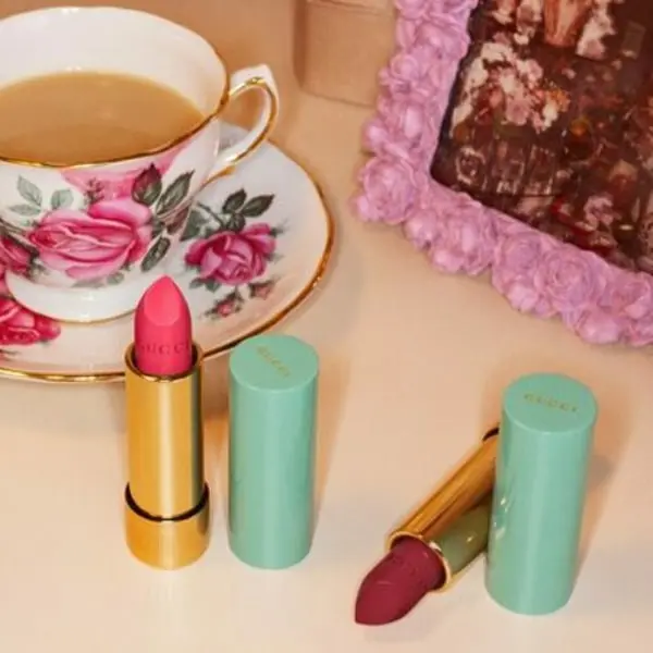 Rouges à lèvres Gucci posés sur une table avec une tasse de thé fleurie à côté d'un cadre rose.