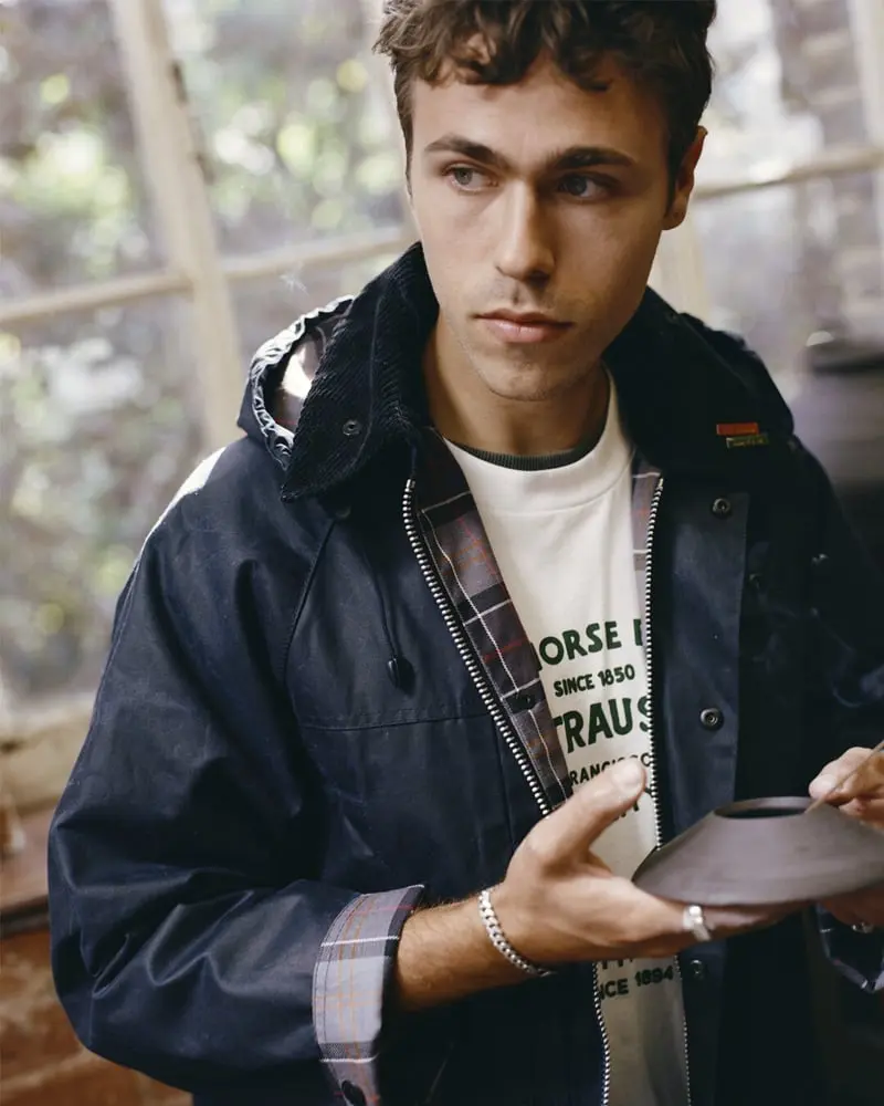 Un homme portant une veste noire et un t-shirt Levi’s observe attentivement un objet rond, devant une fenêtre floue