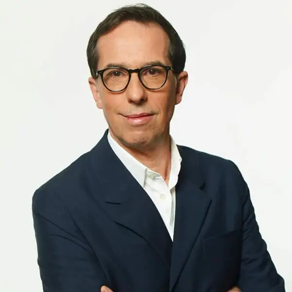 Homme en costume sombre portant des lunettes, fonds clair, représentant L'Oréal dans des discussions stratégiques.