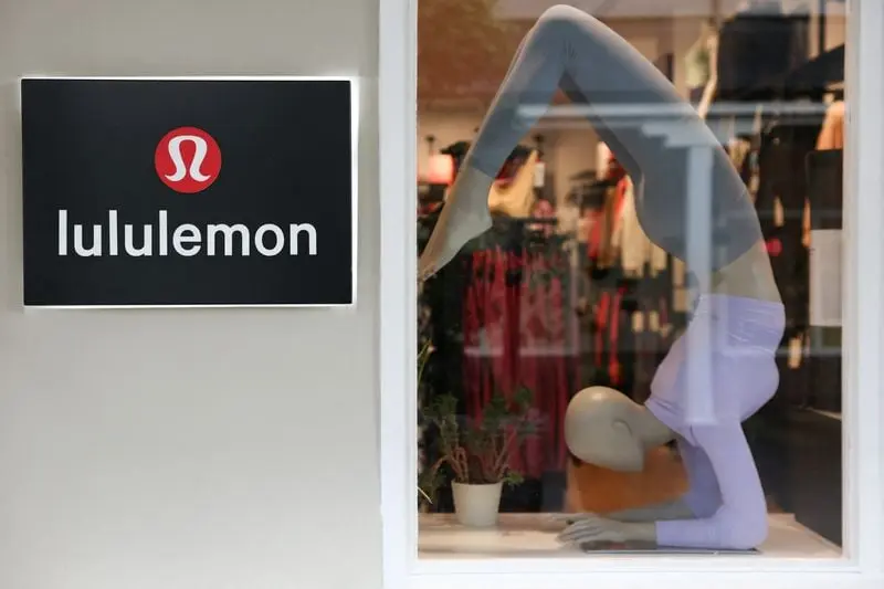 Mannequin en vitrine faisant une pose de yoga sous le logo Lululemon, entouré de plantes et vêtements en arrière-plan
