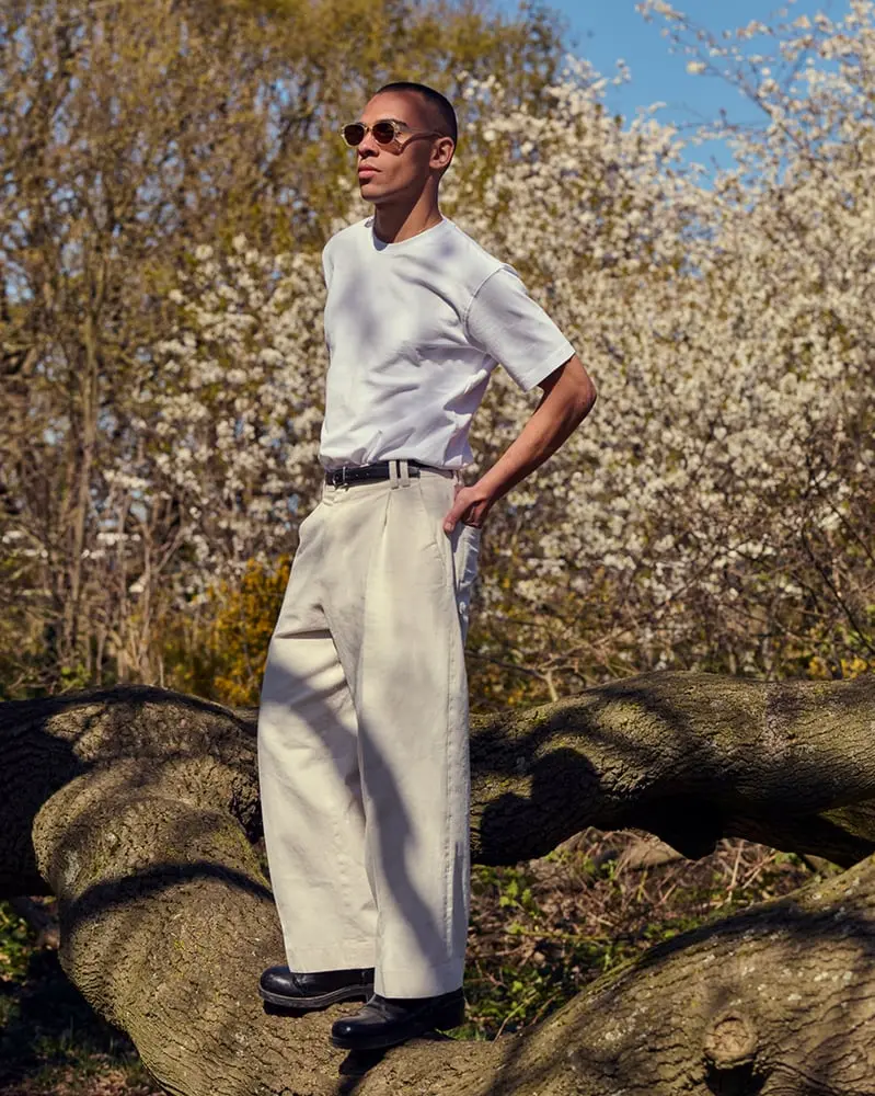 Un homme portant des lunettes Greenwich se tient sur un tronc d'arbre, entouré de fleurs blanches en pleine nature