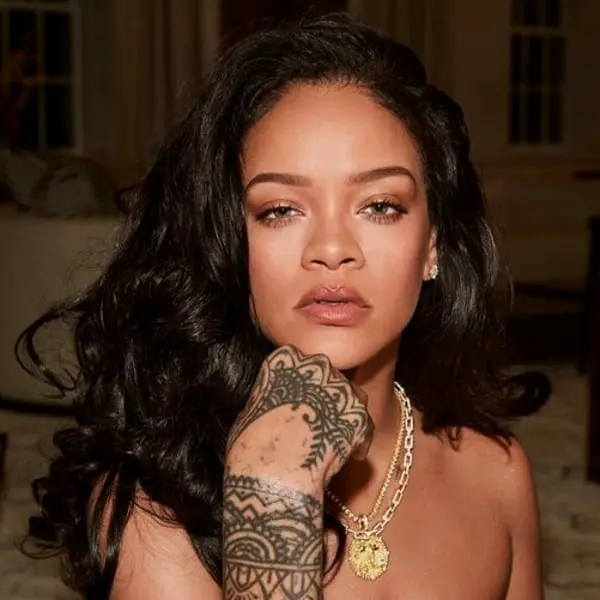 Rihanna posant avec un collier doré et un tatouage sur la main, illustrant sa marque Fenty Beauty
