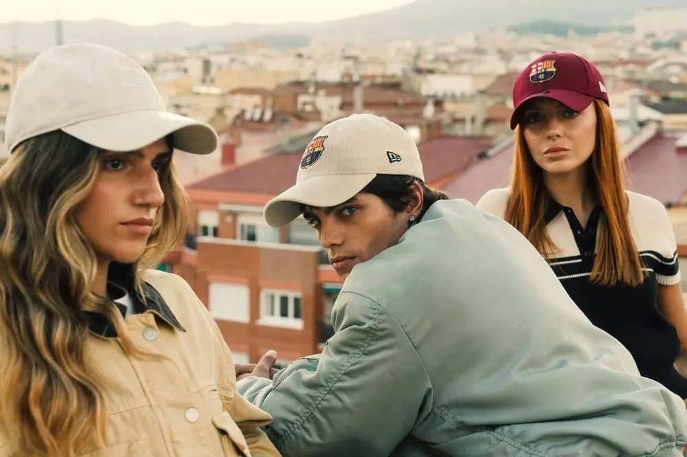 Trois modèles posent avec des casquettes New Era sur un toit urbain, arborant le logo du FC Barcelone