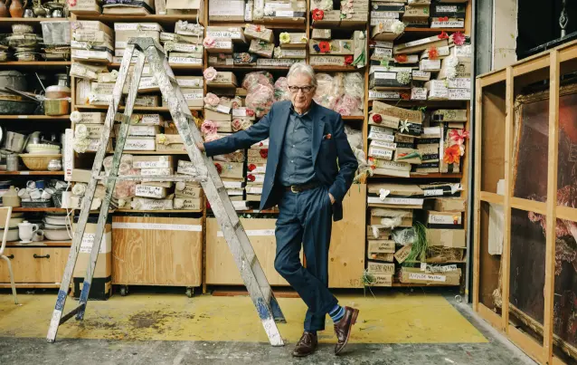 Paul Smith pose dans un atelier devant des étagères remplies de boîtes et de fleurs
