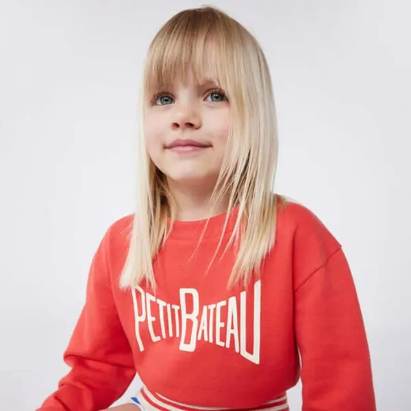 Enfant blonde portant un sweat-shirt rouge avec le logo Petit Bateau