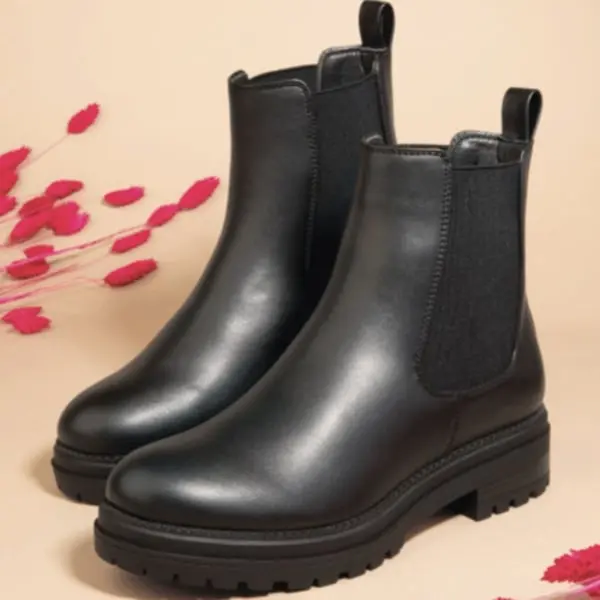 Bottes en cuir noir de Shoe Zone posées sur un fond beige avec des touches de feuillage rouge