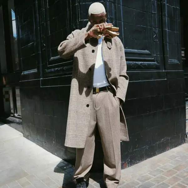 Homme en manteau à carreaux et pantalon assorti, se tient devant un mur sombre, promouvant Topman.