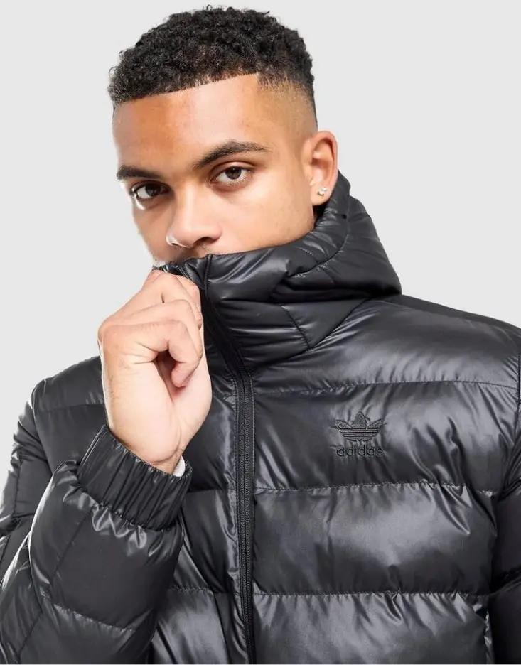 Homme portant une veste noire Adidas, le col relevé, soulignant la popularité des vestes chez JD Sports