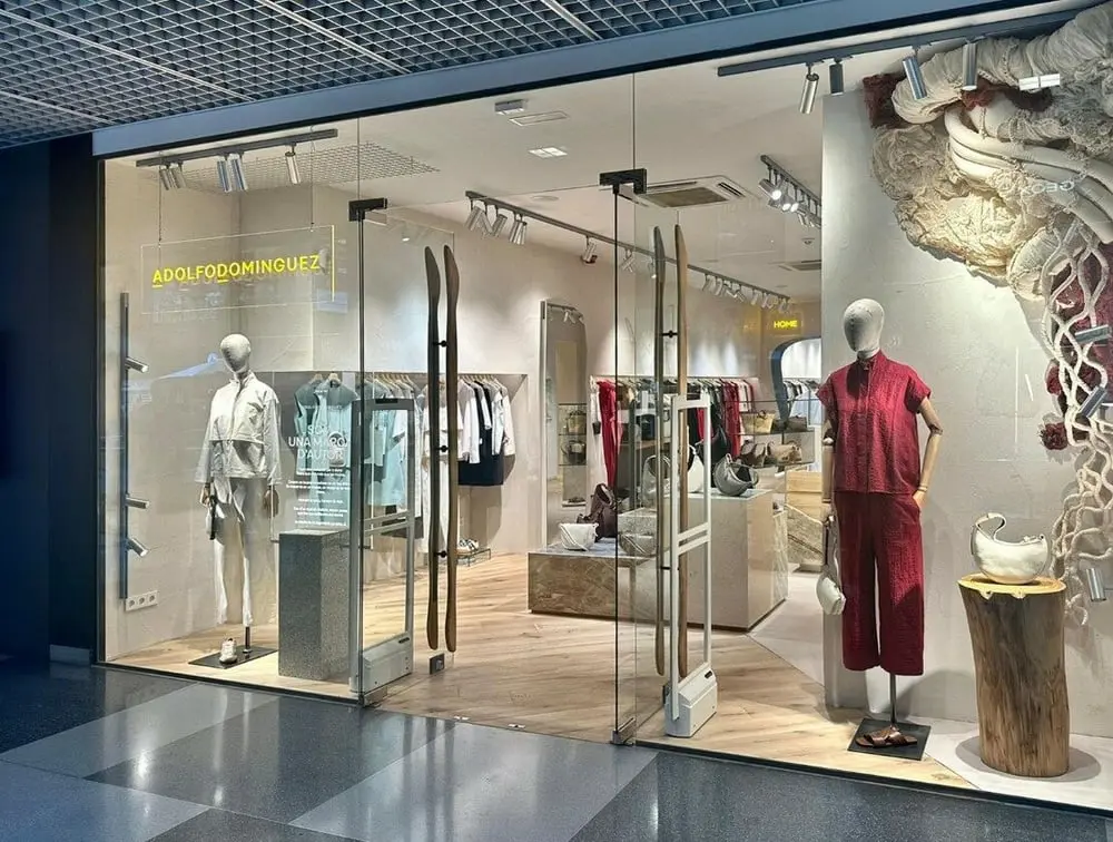 Vitrine d'une boutique Adolfo Domínguez avec mannequins et vêtements exposés à l'intérieur lumineux.
