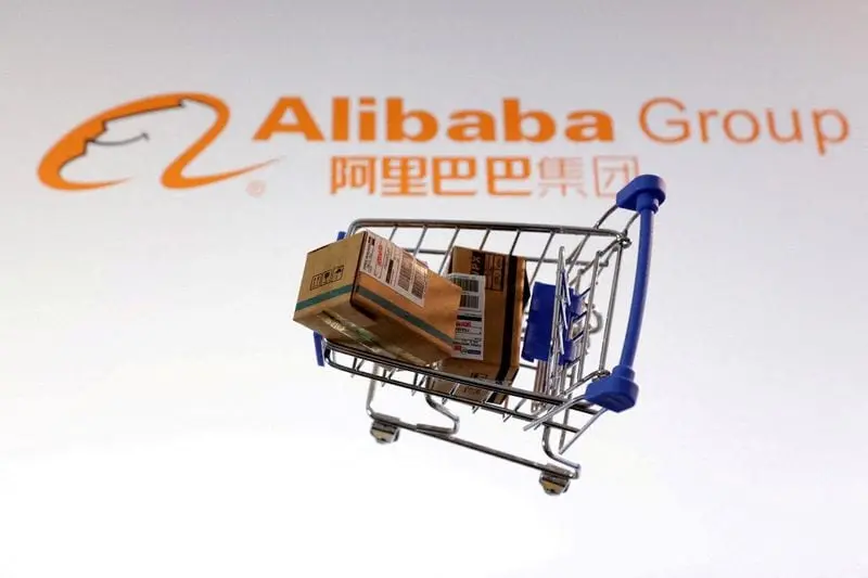 Un chariot miniature avec des colis devant le logo Alibaba mettant en avant l'activité e-commerce du groupe