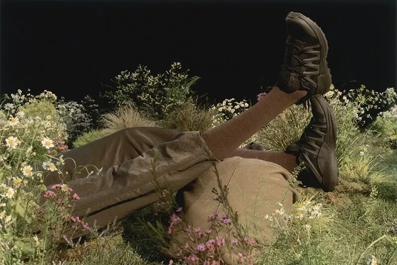 Personne allongée dans l'herbe, pantalon marron clair, chaussures noires, mettant en avant les produits Salomon