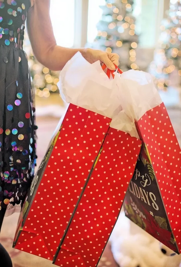 Personne tenant des sacs cadeaux rouges à pois dans un magasin décoré pour les fêtes, préparatifs du Black Friday