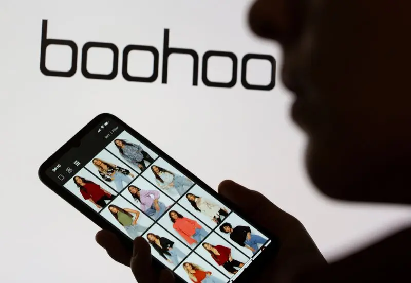 Une personne examine des vêtements sur un smartphone devant un logo Boohoo.