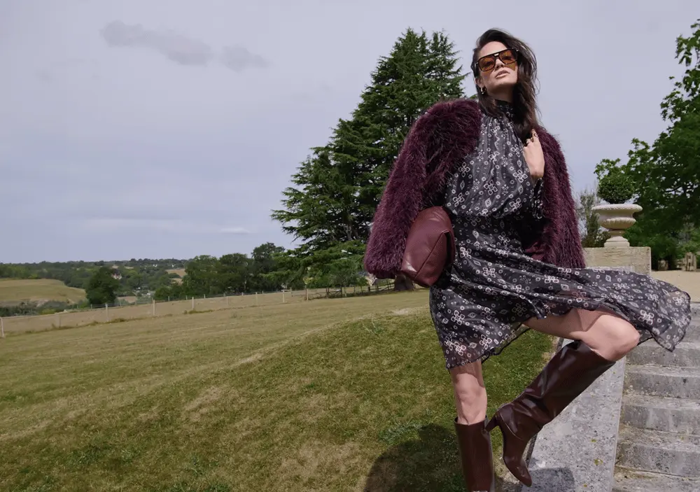 Une femme en robe à fleurs pose sur des escaliers, champs verdoyants en arrière-plan, illustrant l'acquisition de Very Group.