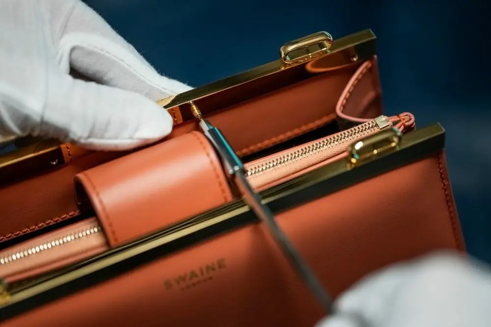 Main en gants travaillant sur un sac à main de luxe avec le logo Swaine, aligné avec la croissance de Chargeurs Invest