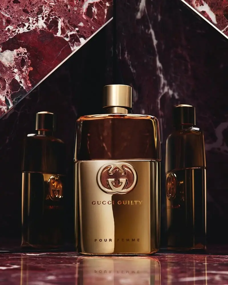 Flacon de parfum Gucci Guilty Pour Femme devant un fond marbré rouge profond avec deux bouteilles en arrière-plan