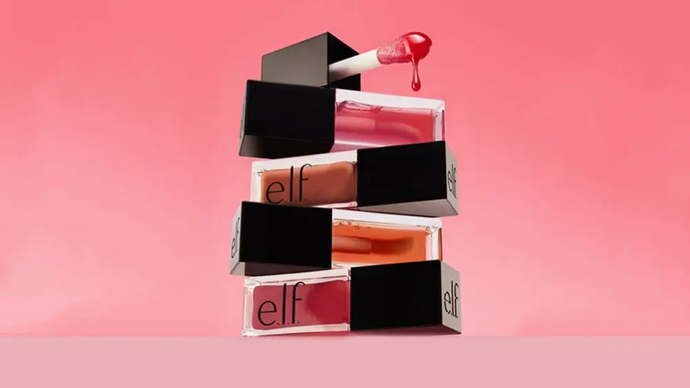 Rouges à lèvres empilés Elf Beauty avec un fond rose et un pinceau débordant de gloss rouge.