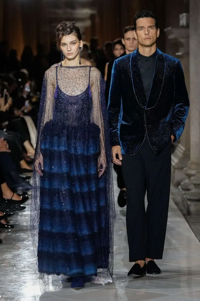 Un modèle défile avec une robe bleue pailletée aux côtés d'un homme en smoking bleu, lors d'un show Giorgio Armani