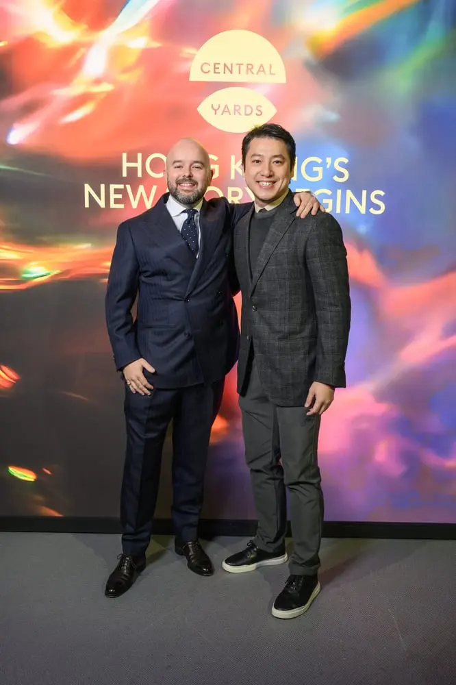 Deux hommes souriants posent devant un panneau lumineux de Central Yards à Hong Kong