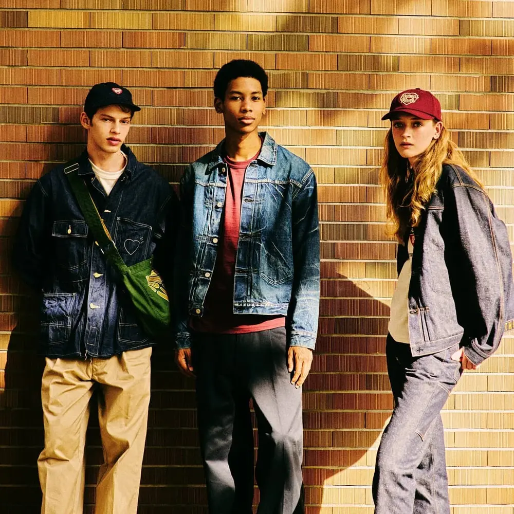 Trois mannequins posent en vêtements Human Made devant un mur en briques dans une ambiance urbaine et décontractée