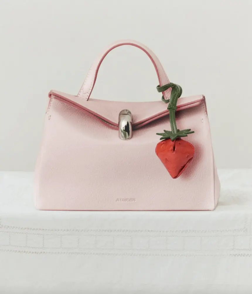 Sac rose Jacquemus Le Valérie avec une décoration fraise rouge sur une table blanche