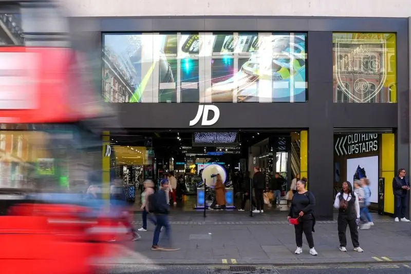 Façade du magasin JD Sports avec des passants flous et un bus rouge en mouvement devant l'entrée