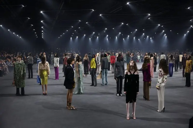 Des mannequins présentent des tenues variées sur une scène éclairée, illustrant un soutien à Valentino.