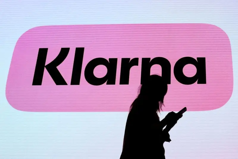 Silhouette d'une personne utilisant un téléphone devant le logo rose de Klarna