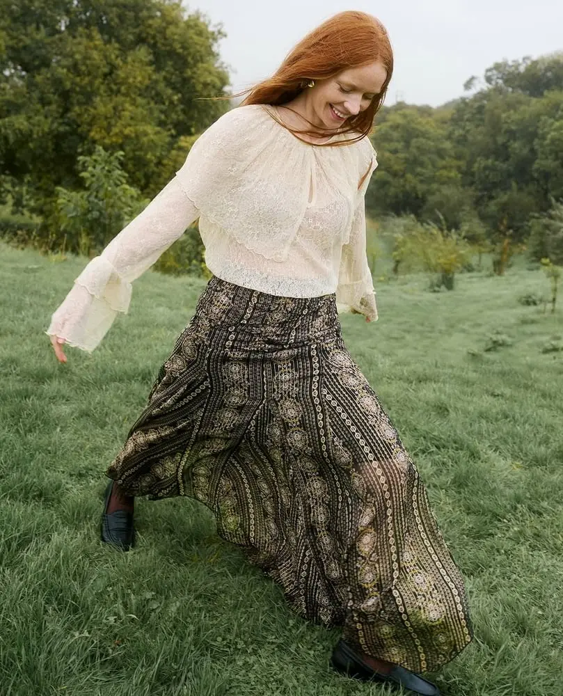 Une femme souriante portant une jupe longue de Monsoon Accessorize marche dans un champ verdoyant.