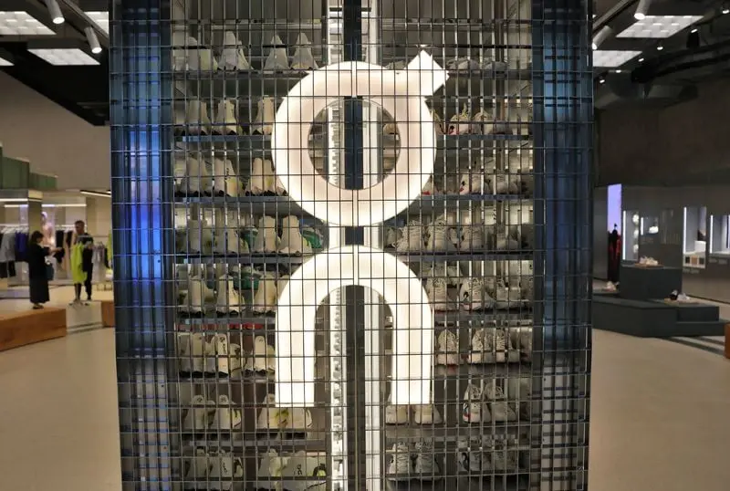 Logo d'On Holding sur une grille métallique devant des étagères remplies de chaussures dans un magasin moderne