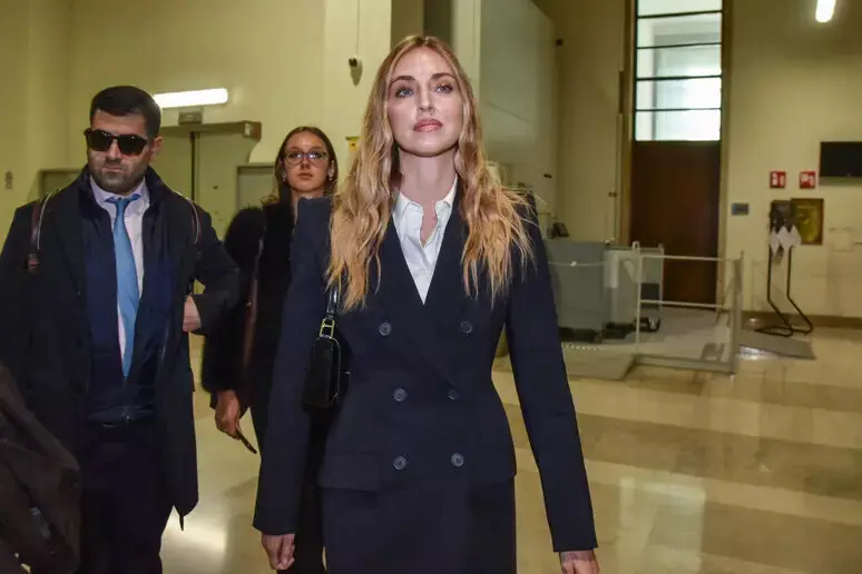 Chiara Ferragni en costume sombre dans un bâtiment institutionnel à Milan, entourée de deux personnes.