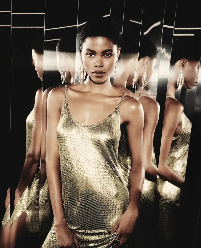 Modèle en robe dorée scintillante de Rabanne, entourée de miroirs lors de la présentation VIP de la capsule exclusive