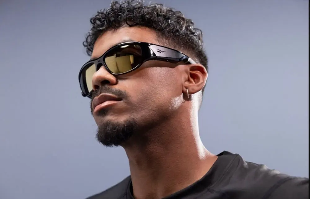 Homme portant des lunettes de soleil Reebok avec monture noire, fond bleu clair