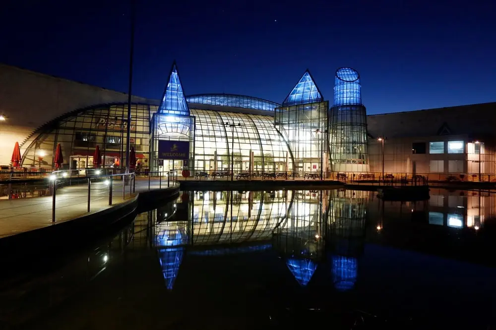 Bâtiment moderne de Landsec éclairé la nuit se reflétant dans l'eau, avec structures en verre illuminées et ciel bleu foncé