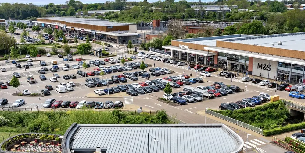 Parking bondé devant un retail park avec enseignes M&S et Homesense, accentuant l'importance de British Land