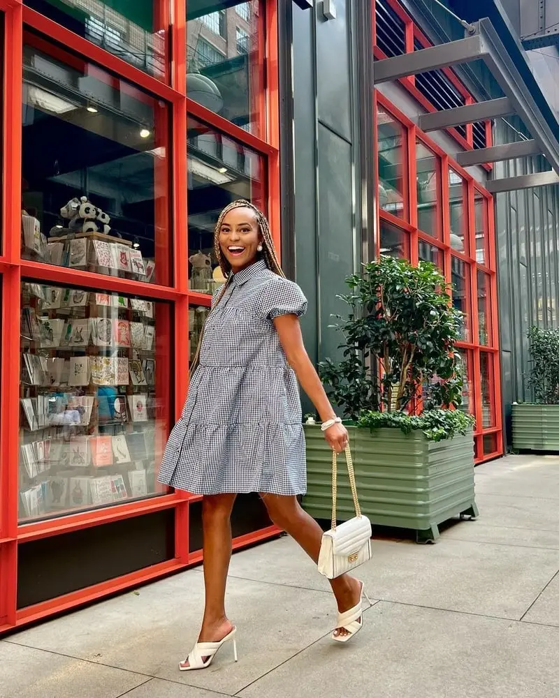 Une femme souriante marche devant une vitrine colorée, portant une robe à carreaux et des sandales, symbole tendance de Ross Stores