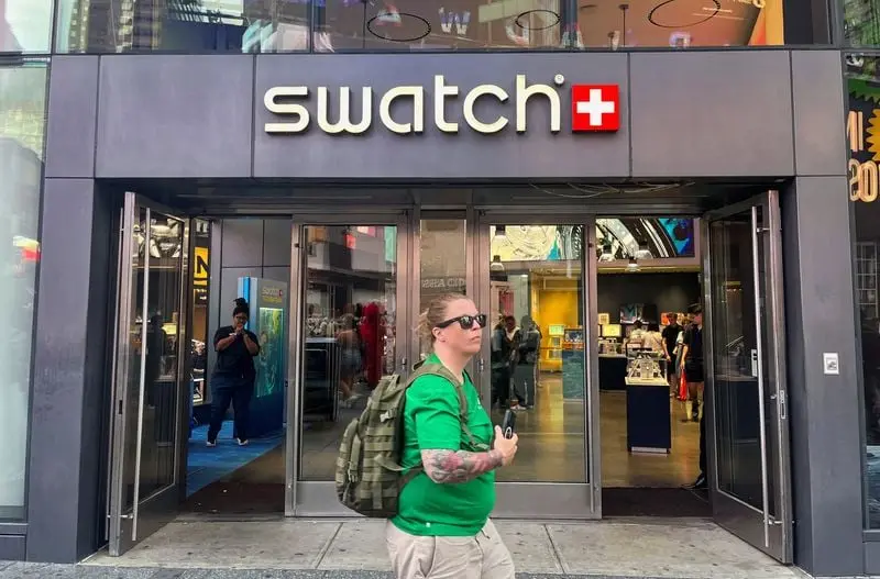 Façade d'une boutique Swatch avec une personne passant devant l'entrée, vitrine lumineuse à l'intérieur.
