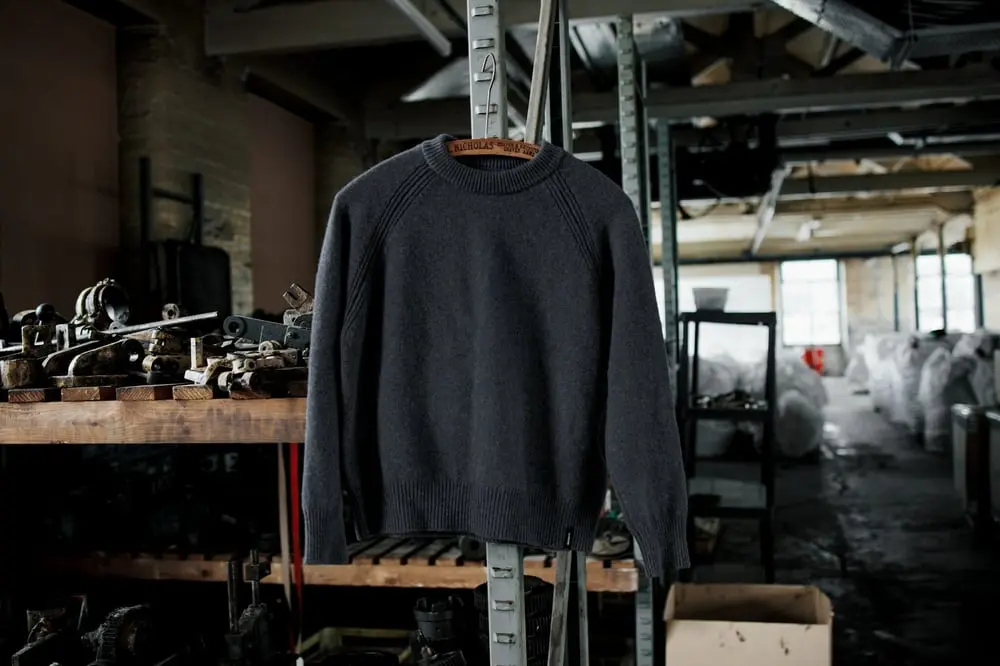 Sweat gris en laine circulaire de Finisterre suspendu dans un atelier industriel avec des machines en arrière-plan