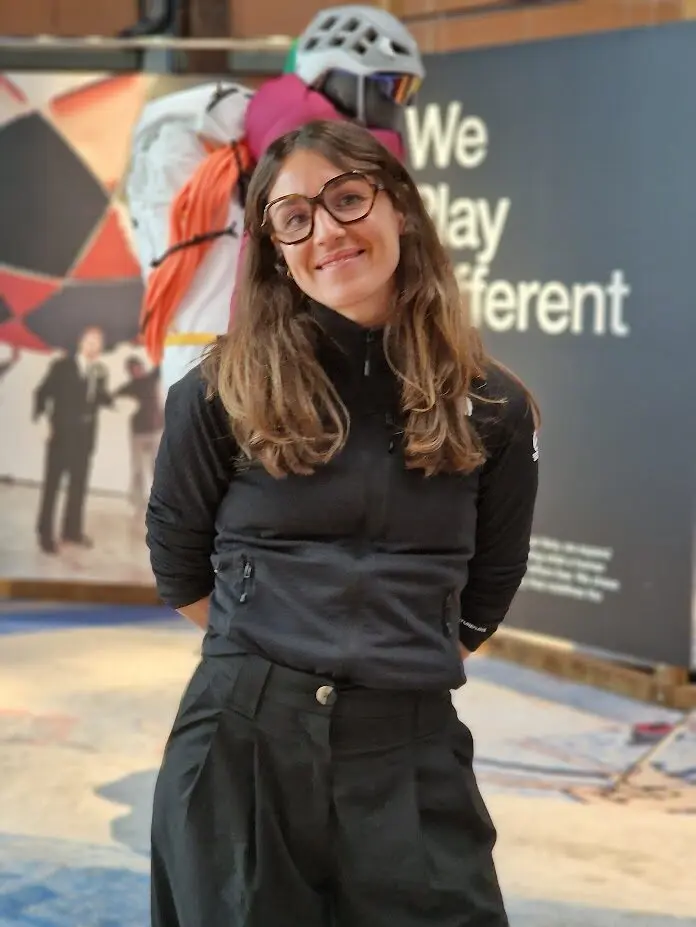 Une femme souriante devant un panneau avec le slogan "We play different" chez The North Face.