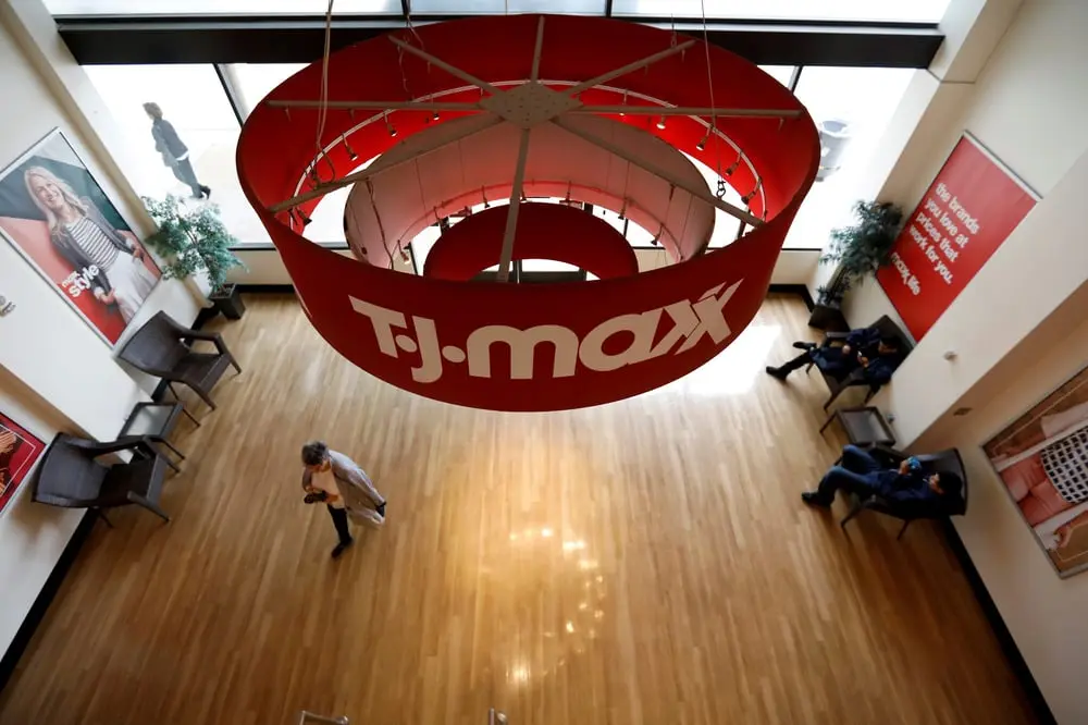 Une affiche TJ Maxx suspendue dans un magasin, avec des clients marchant sur un sol en bois clair