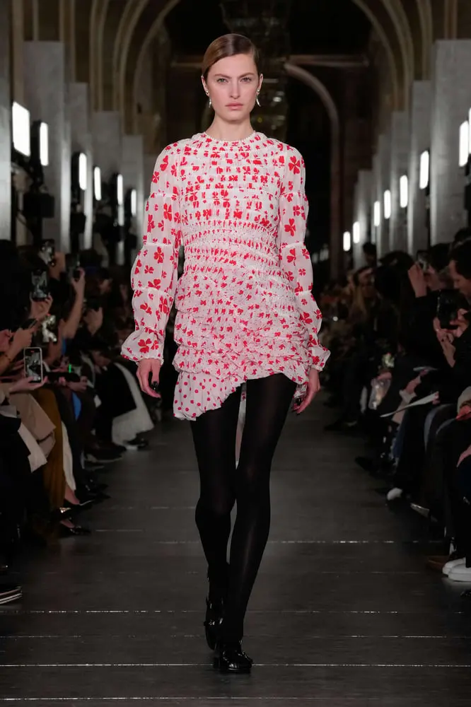 Mannequin défilant dans une robe à motifs rouges lors d'un show de mode Tory Burch dans un cadre élégant