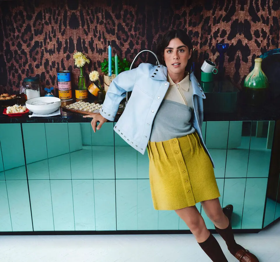 Femme en jupe jaune et veste claire posant devant un comptoir avec des objets rétro, inspirée des années 60 pour Parfois