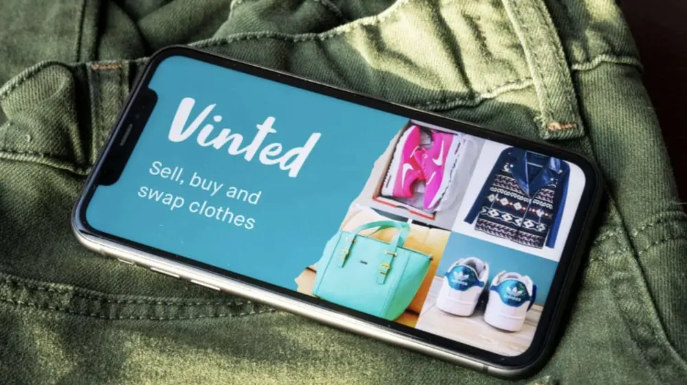 Vinted sur un smartphone affichant des articles de mode variés posés sur un tissu vert