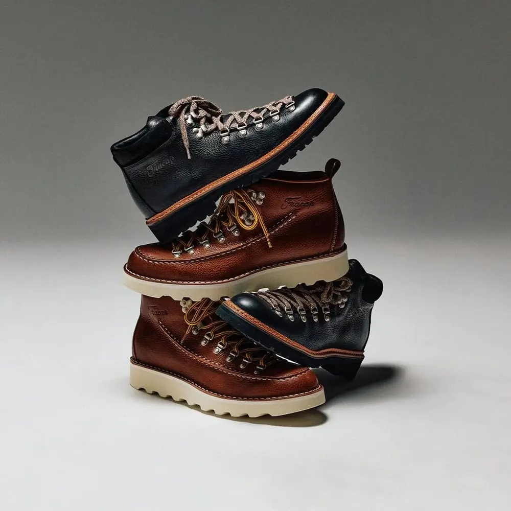 Des bottes en cuir Fracap Italie, noires et marron, empilées artistiquement sur fond neutre.