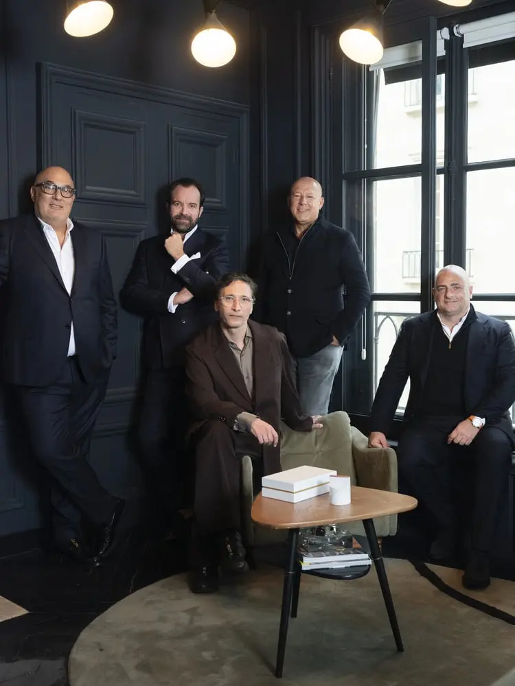 Cinq hommes en costume posent dans une pièce élégante, symbolisant la fusion de WMH Project pour The Officin luxe