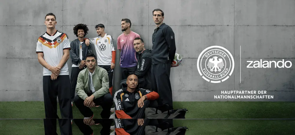 Joueurs de football posant avec des vêtements sportifs, logo Zalando visible, sur fond de mur gris et herbe verte